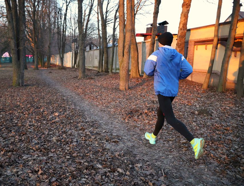 A person runs along a leaf-strewn path in an autumn park, wearing bright athletic gear.