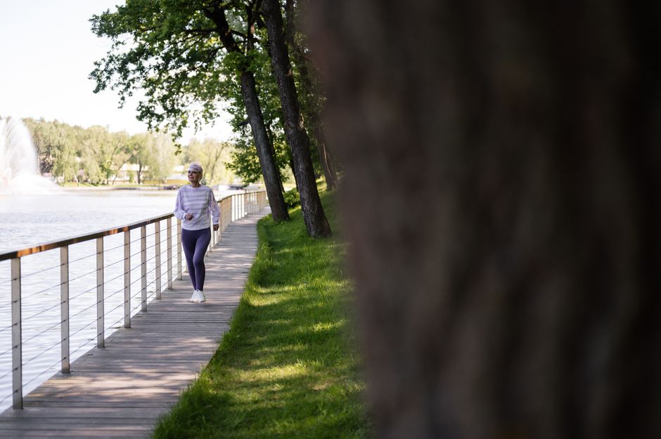 A senior woman enjoys a healthy walk on a lakeside boardwalk on a sunny day.