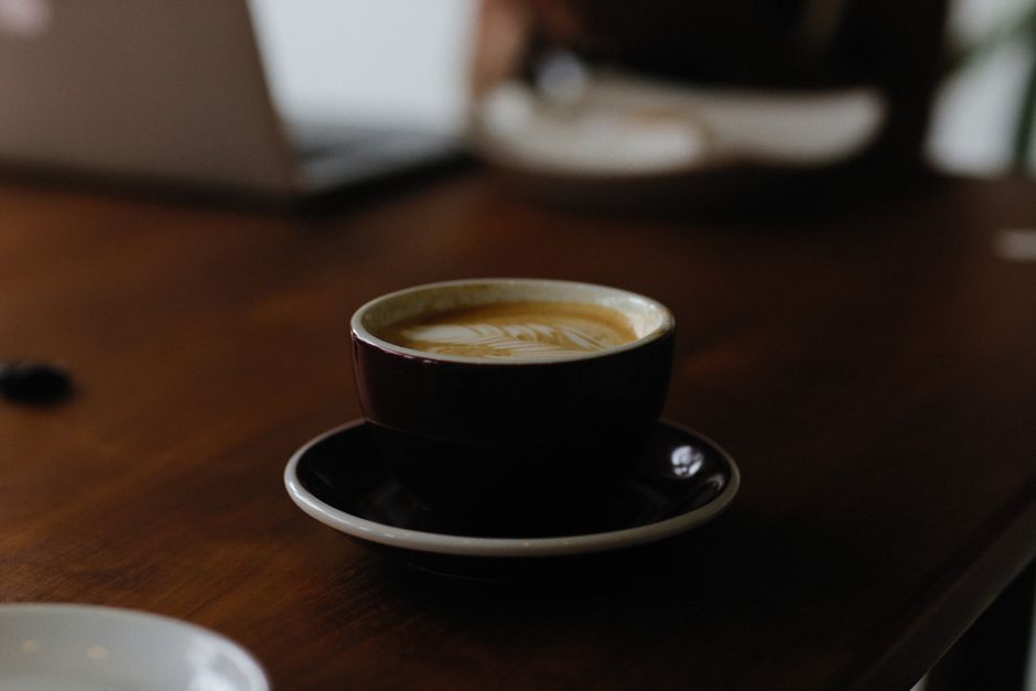 A steaming cup of espresso sits on a wooden table, offering a cozy coffee shop vibe.