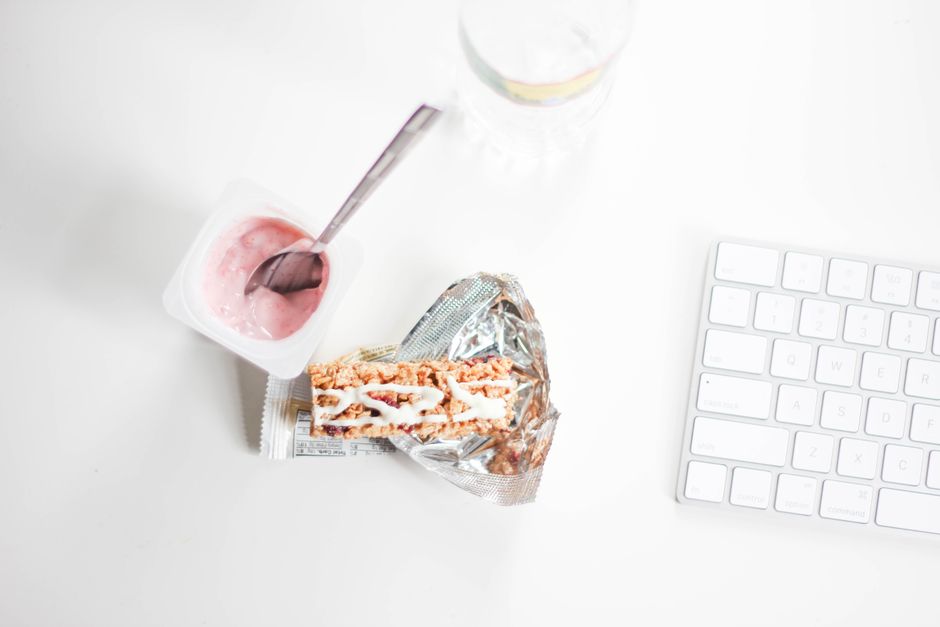 A stylish flat lay of yogurt and granola bar on a desk, perfect for a quick healthy snack.