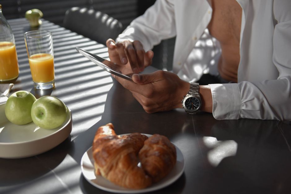 A stylish morning setup featuring a croissant, apples, orange juice, and a tablet in an elegant indoor setting.