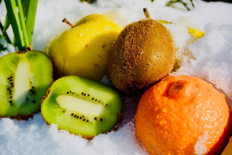 A vibrant mix of kiwi, orange, and apple on snow, showcasing fresh produce.