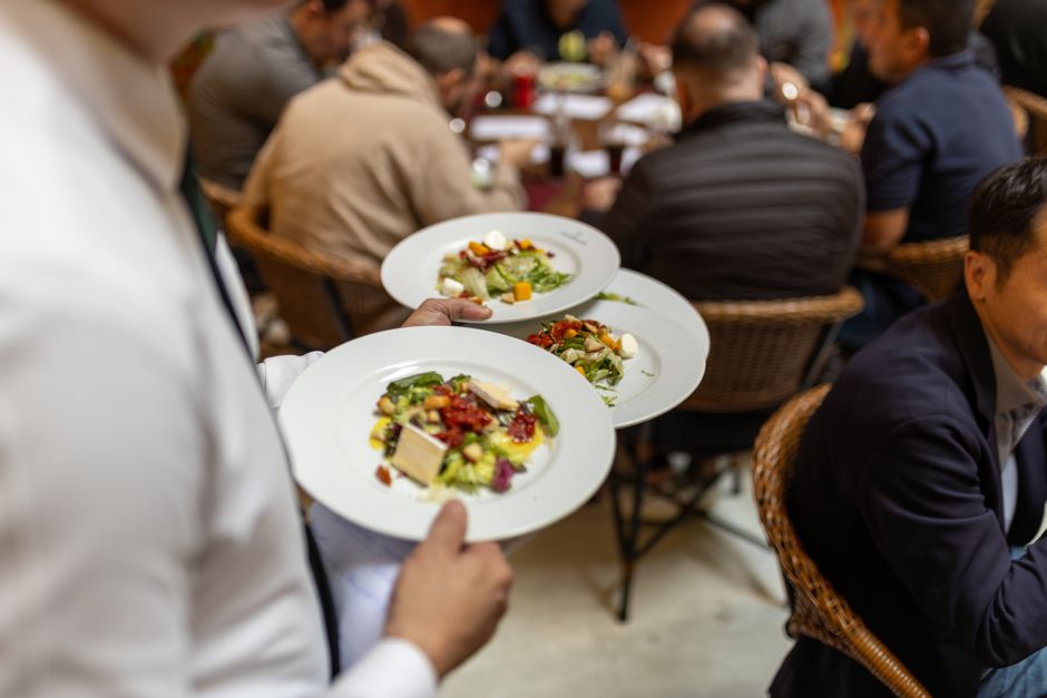 A waiter serves gourmet salads to a group of diners in a lively restaurant setting.