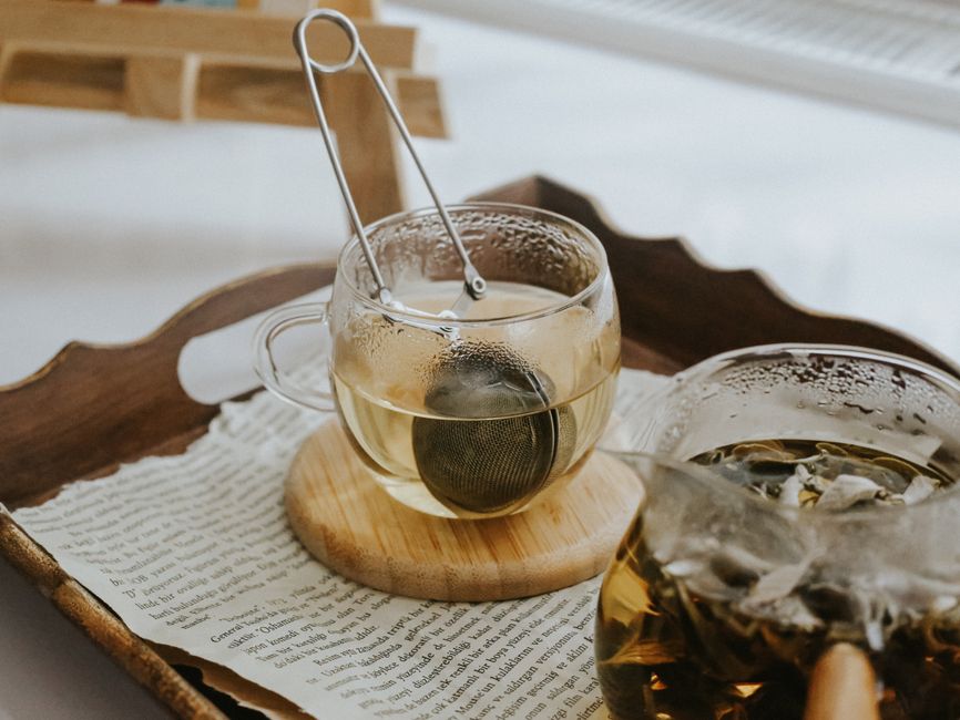 A warm, cozy scene showcasing glass teacups with tea infuser on a tray with scattered papers.