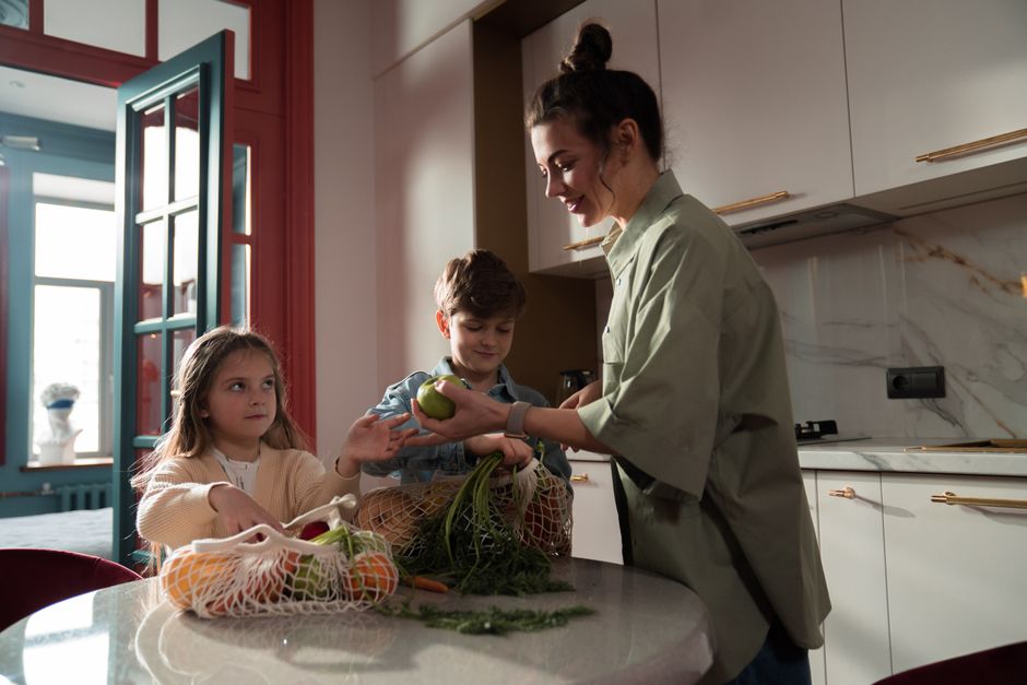 A woman and children preparing fresh vegetables in a modern kitchen, enjoying family time.