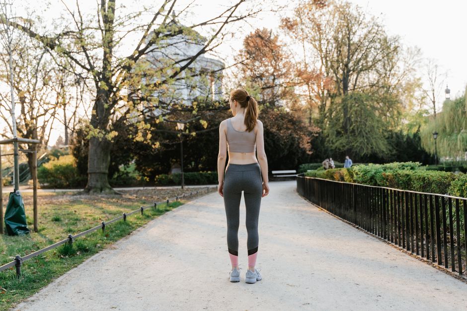 A woman in activewear walks along a path in a sunny park, showcasing fitness in nature.