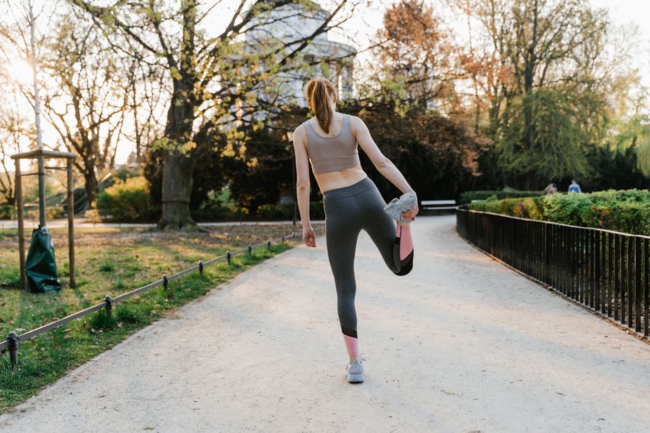 A woman performs a stretching exercise in a park setting, showcasing fitness and a healthy lifestyle.