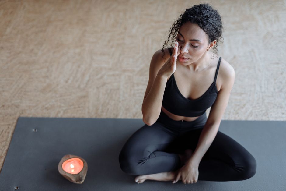 A woman practicing meditation on a yoga mat, focusing with eyes closed next to a candle indoors.