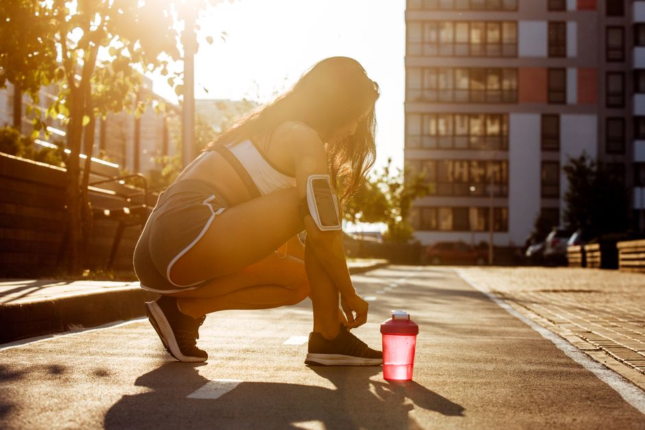 A woman preparing for a workout outdoors during the golden hour, tying her shoes on a city street.