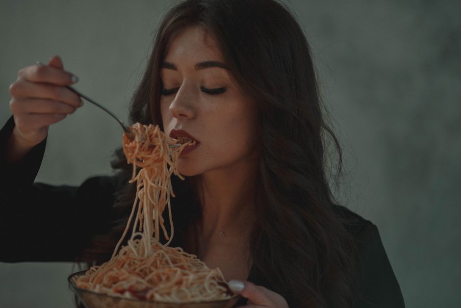 A woman relishes a forkful of spaghetti pasta in a cozy indoor setting, conveying warmth and indulgence.