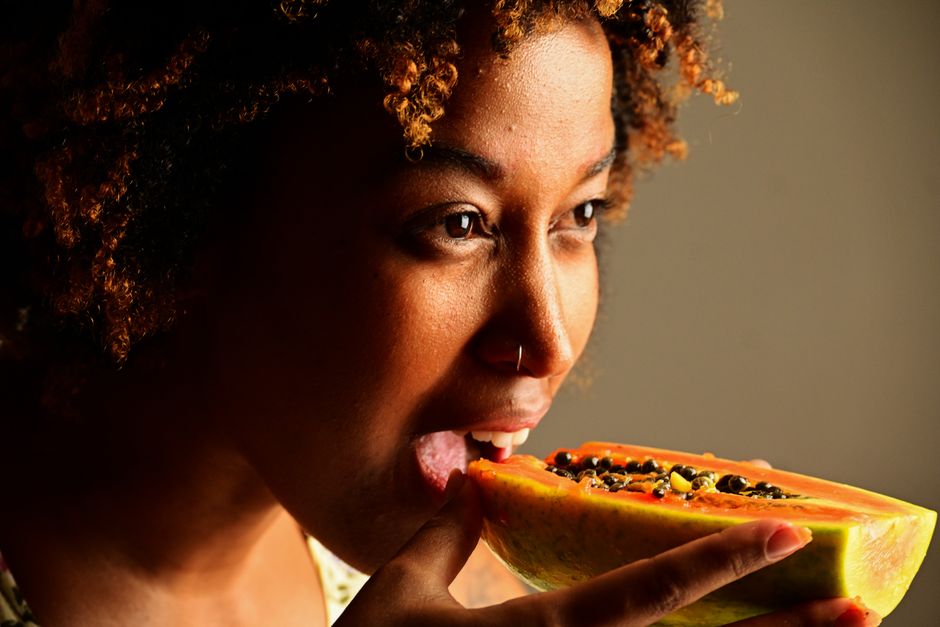 A woman savoring a papaya slice, highlighting natural textures and vibrant colors.
