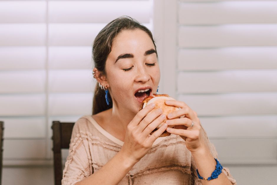 A woman savoring a sandwich in a comfortable indoor setting with closed eyes.