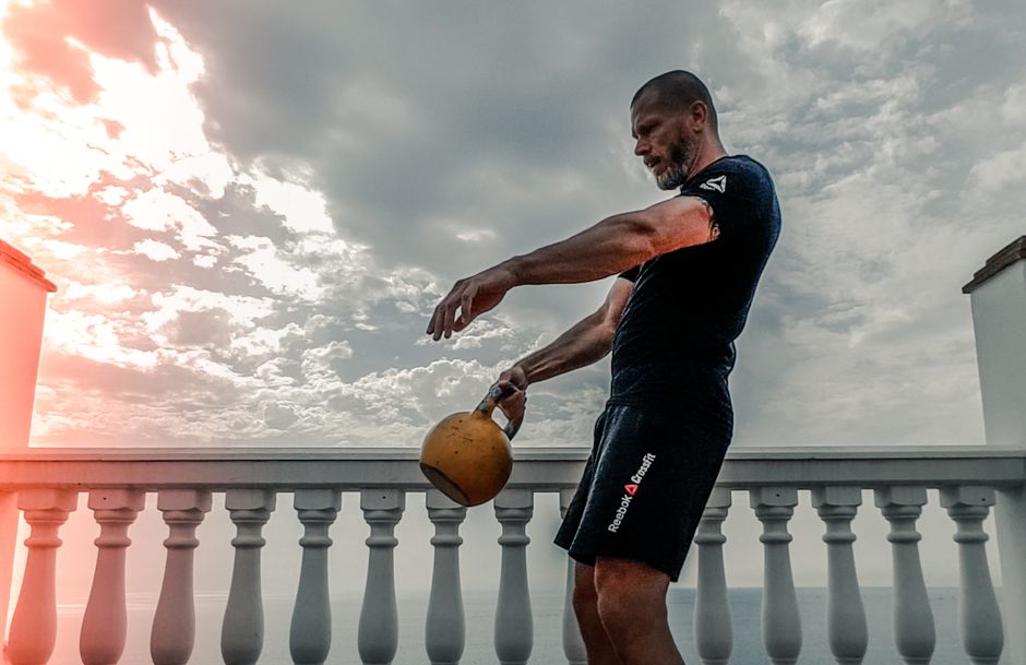 Adult male performing a kettlebell workout on a terrace under a cloudy sky.