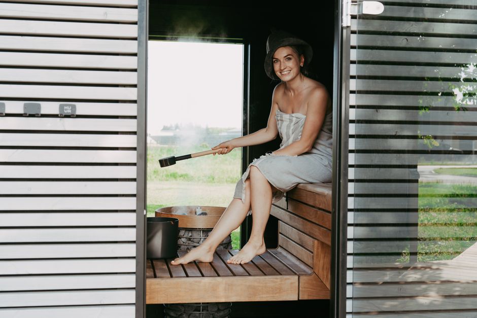 Adult woman in a sauna wearing a towel and hat, seated on a bench, enjoying a relaxed moment.