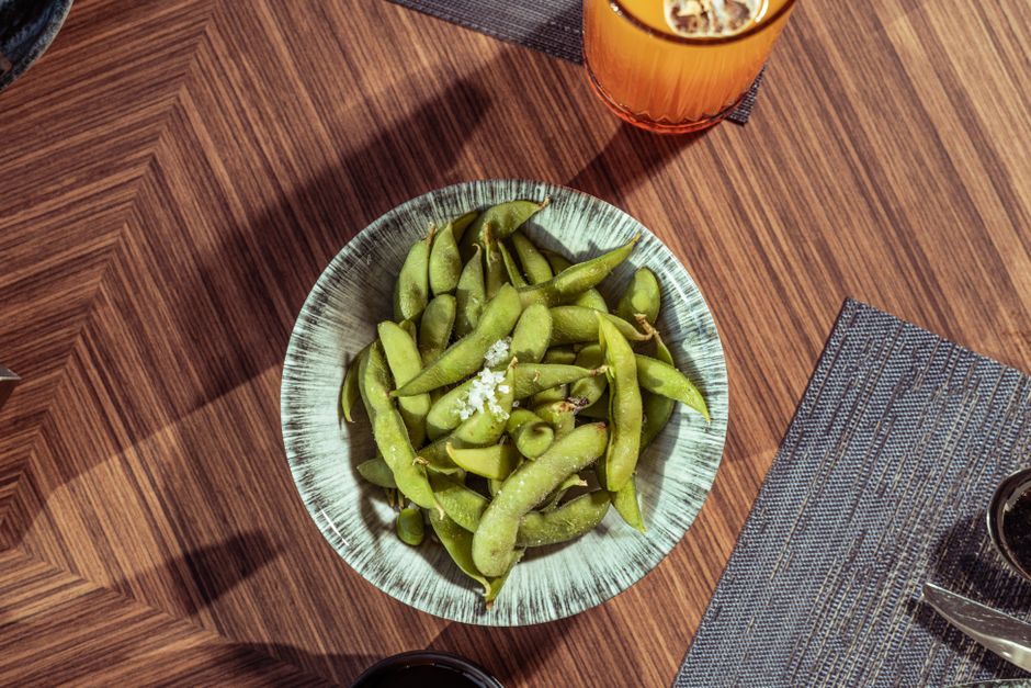 Aerial view of fresh edamame sprinkled with salt in a bowl, placed on a stylish wooden table in a modern setting.
