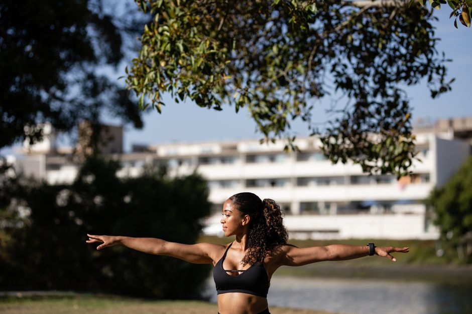 African American woman in activewear doing yoga in a sunny outdoor park setting.