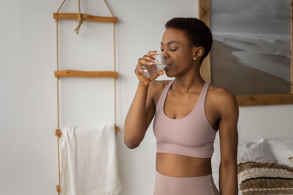 African American woman in sports bra drinking water from glass indoors.