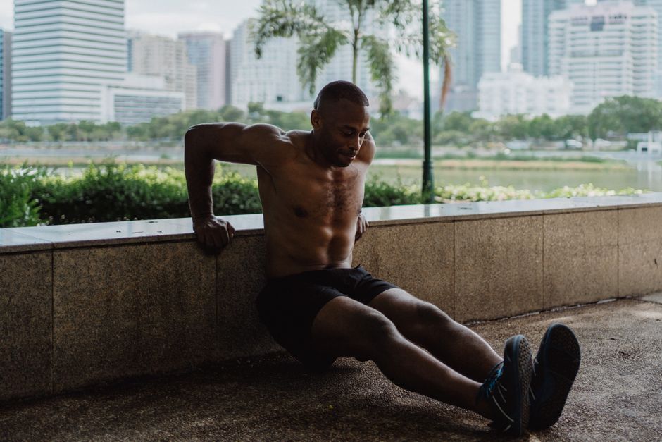 An athletic man engages in a tricep dip workout in an urban park setting.