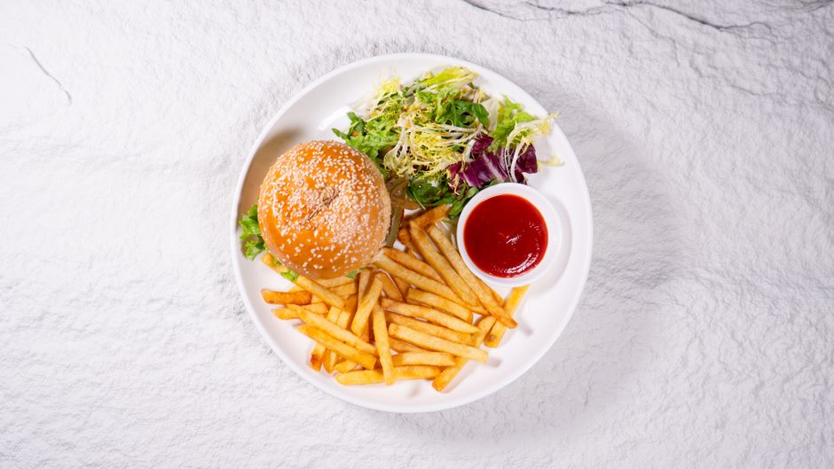 Appetizing burger with crispy fries and fresh salad served on a white plate.