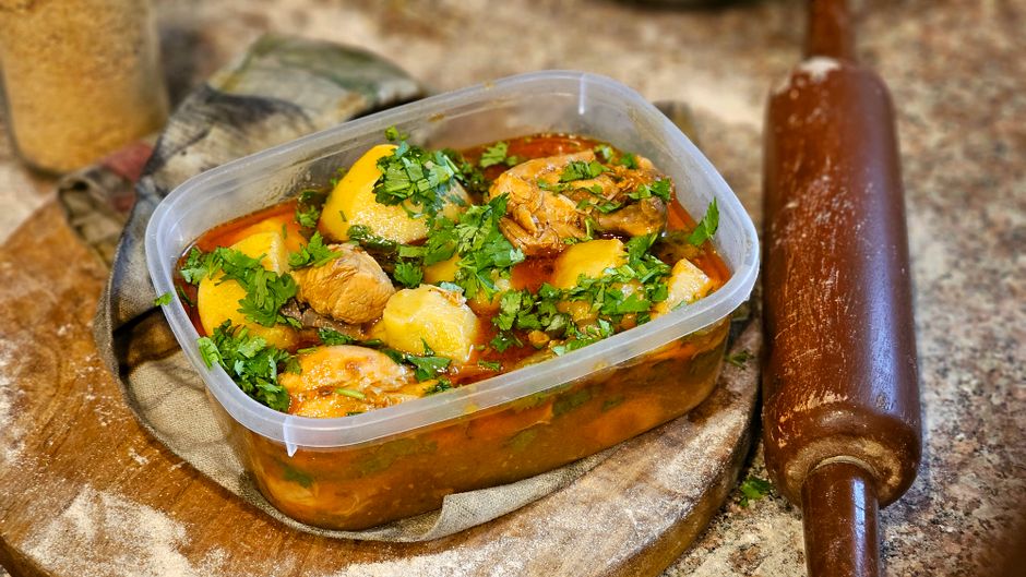 Aromatic homemade chicken stew with herbs and vegetables in a plastic container.