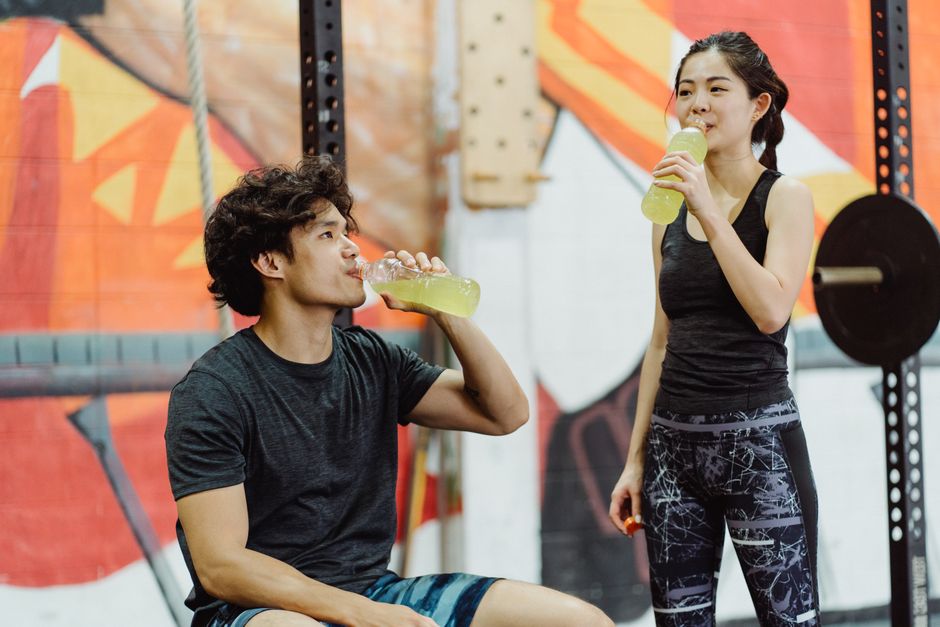 Asian couple in gym attire drinking energy drinks after workout. Vibrant and lively setting.