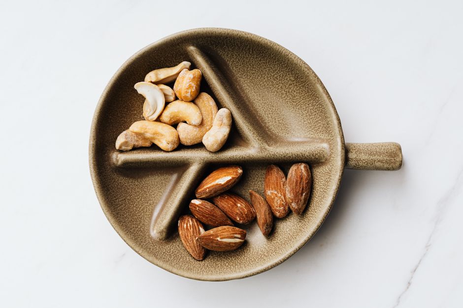 Assortment of cashews and almonds presented on a decorative ceramic plate against a clean white background.