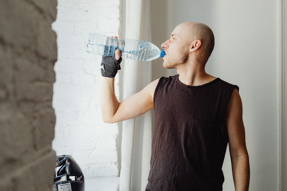 Bald man drinking bottled water indoors, embracing a healthy lifestyle.