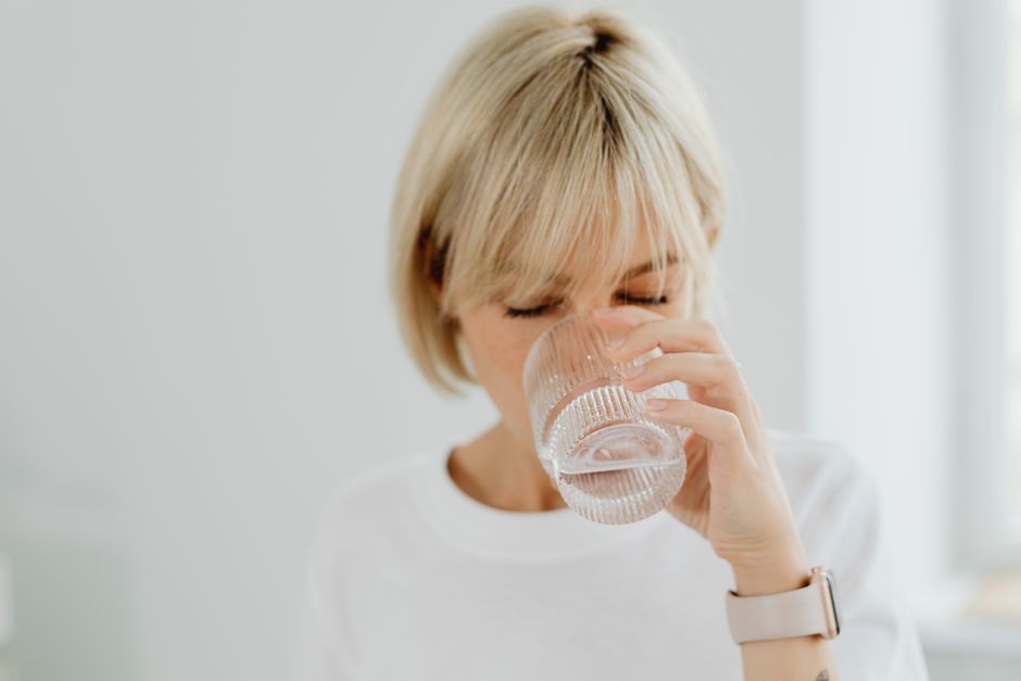 Blonde woman drinking water from glass indoors, showcasing healthy lifestyle and hydration.