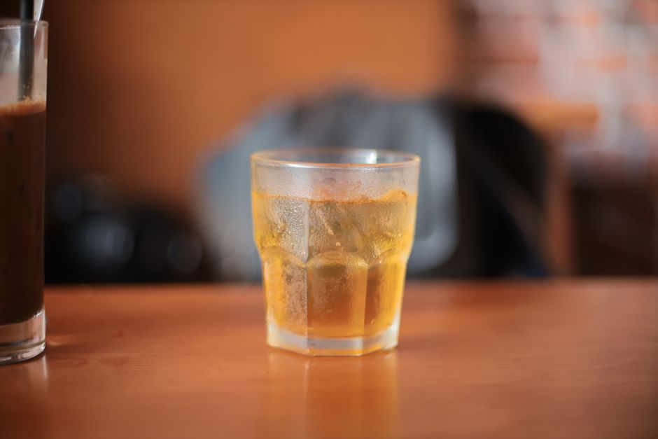 Chilled drink with ice cubes in a glass on a wooden table with blurred cafe background.