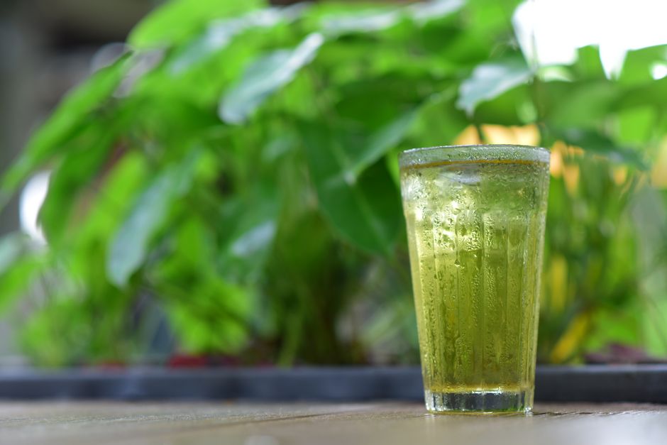 Chilled glass of matcha green tea with ice, set against a blurred green background.