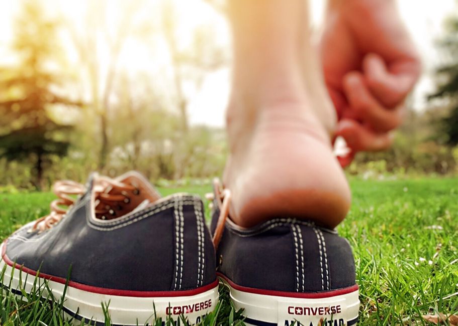 Close-up of a barefoot person stepping into converse sneakers on grass in summer.