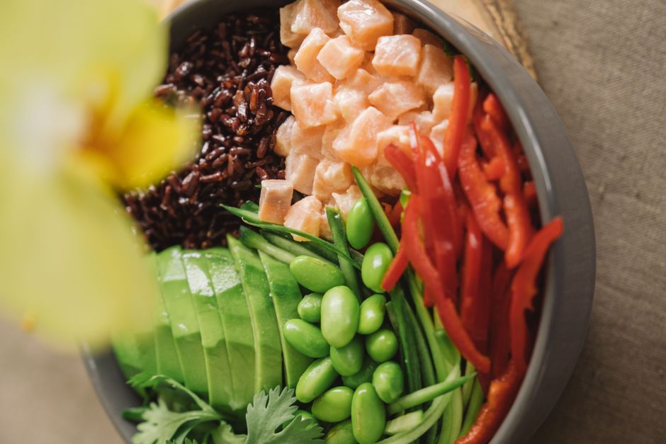 Close-up of a colorful salmon poke bowl featuring avocado, red peppers, and black rice.