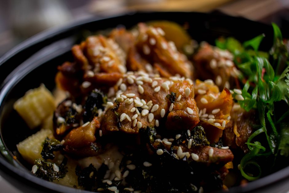 Close-up of a delicious Asian chicken dish topped with sesame seeds and garnished with fresh herbs.