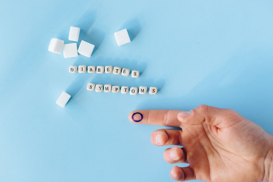 Close-up of a hand with marked finger pointing to diabetes symptoms text and sugar cubes.
