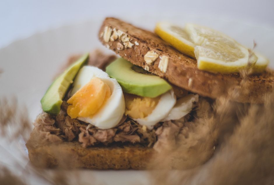 Close-up of a healthy avocado, tuna, and egg sandwich with lemon slices.