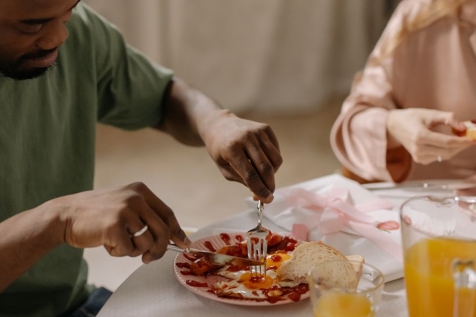 Close-up of a man using a fork and knife to eat a breakfast of eggs, sausage, and bread.