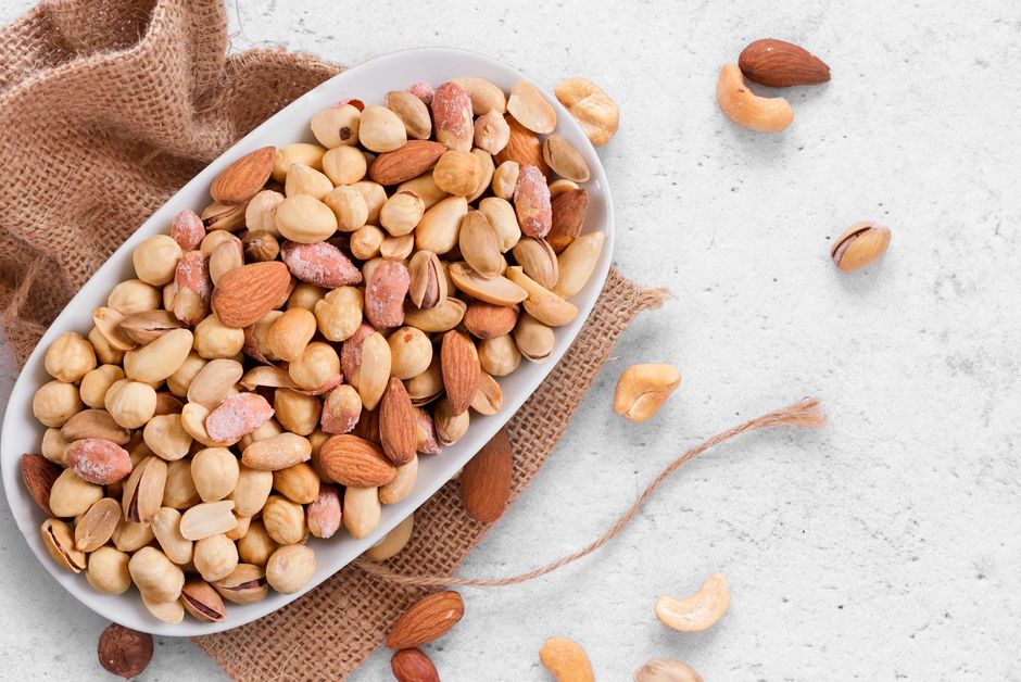 Close-up of a variety of nuts in a white bowl on burlap cloth, offering healthy snack options.