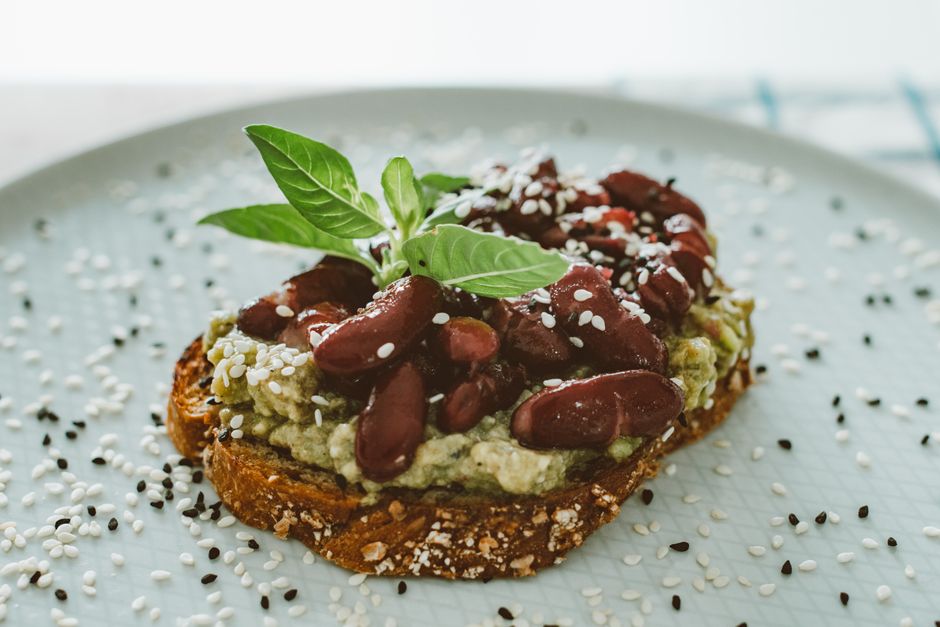 Close-up of a vibrant avocado toast topped with kidney beans and sesame seeds, garnished with fresh basil leaves.
