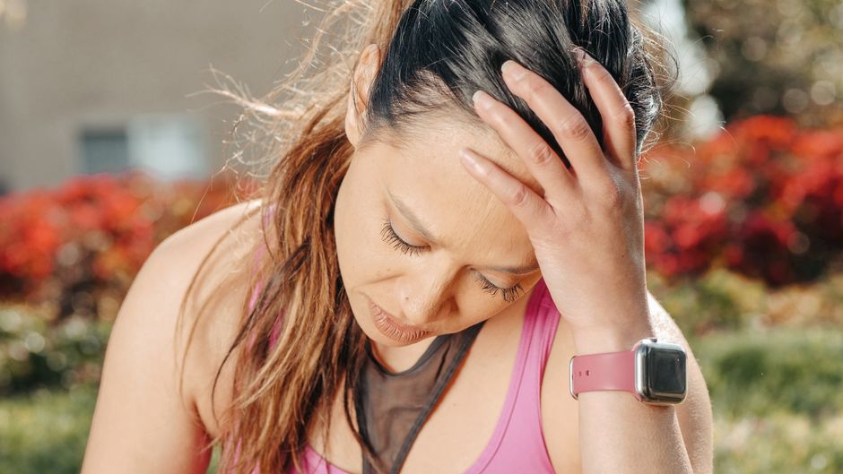 Close-up of a woman with a headache sitting outdoors wearing a smartwatch.