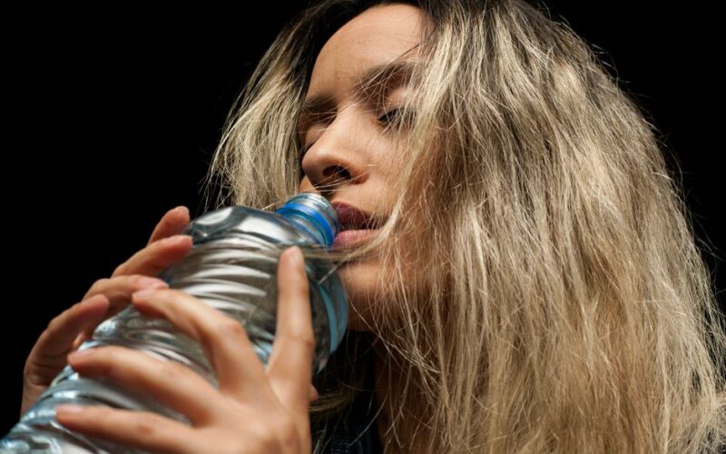 Close-up of a young woman with blond hair drinking from a plastic bottle.