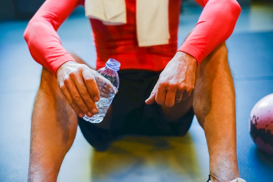 Close-up of an athlete resting with a water bottle in a gym setting.