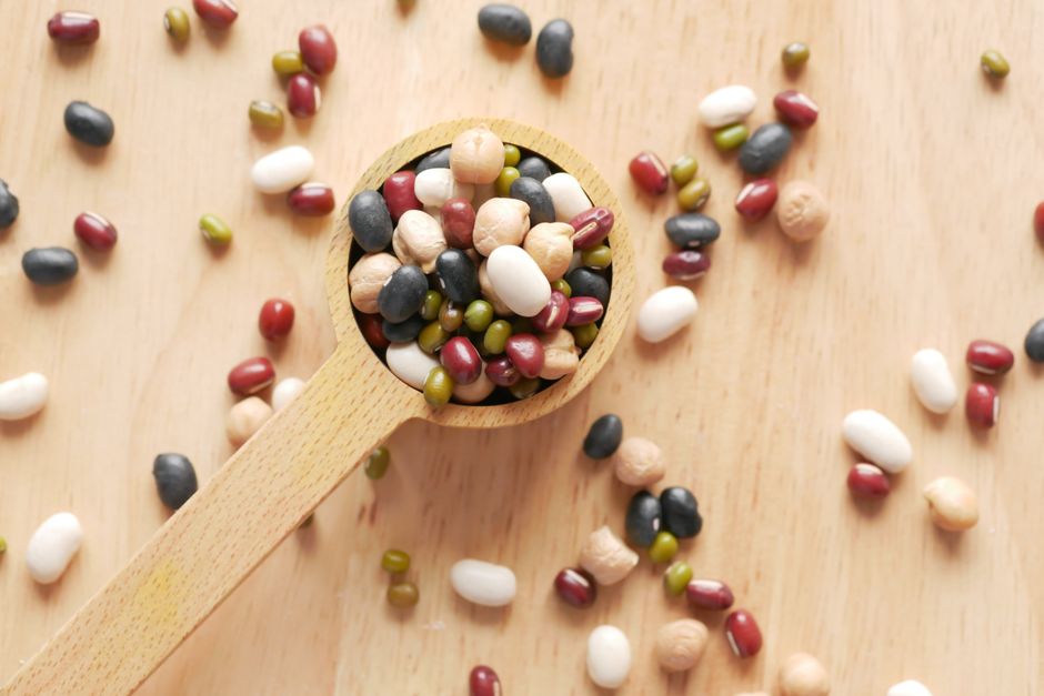 Close-up of assorted beans and legumes on a wooden spoon, showcasing diversity in food ingredients.