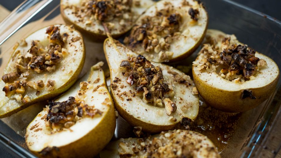 Close-up of baked pear halves topped with nuts and spices in a glass dish, perfect for dessert.