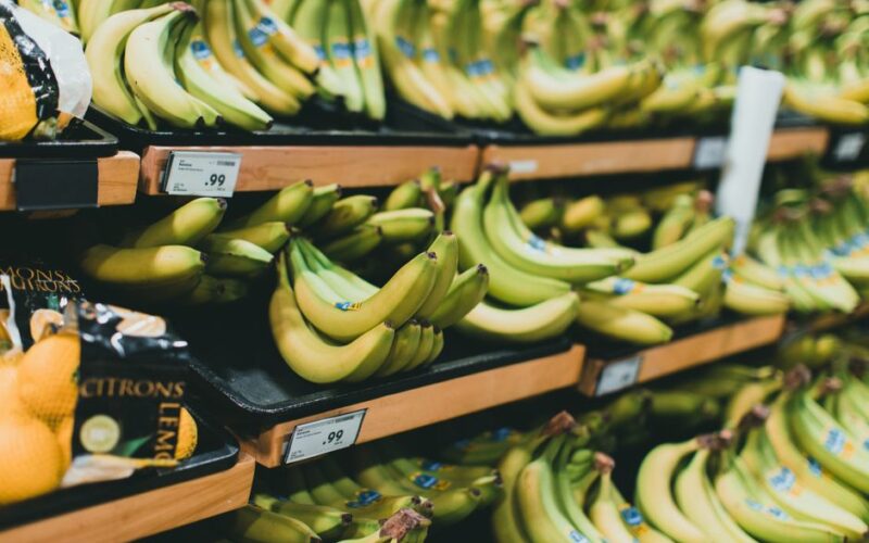 Close-up of fresh bananas stacked on grocery store shelves with price tags visible.