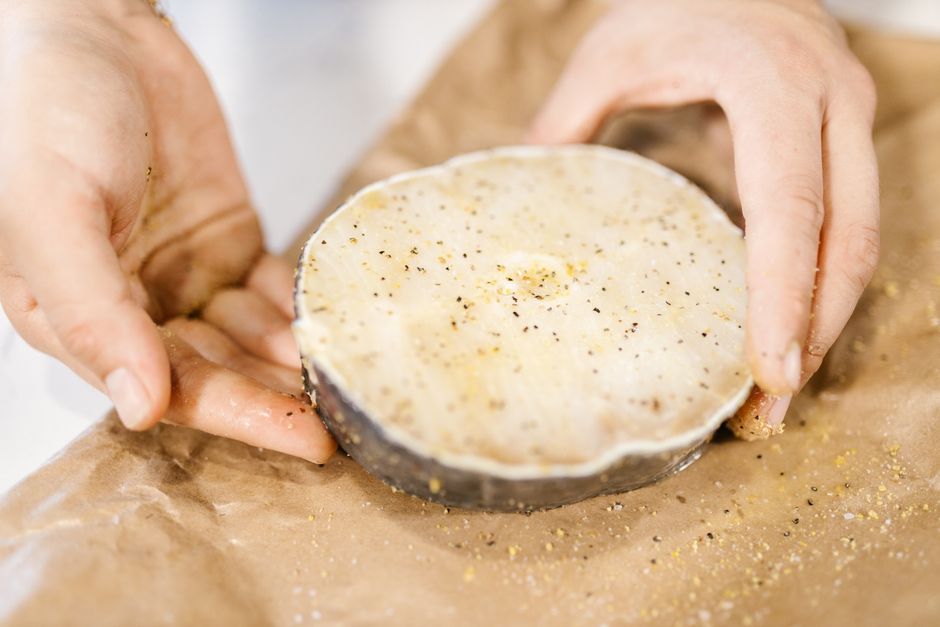 Close-up of hands holding a seasoned fresh fish fillet on brown paper.
