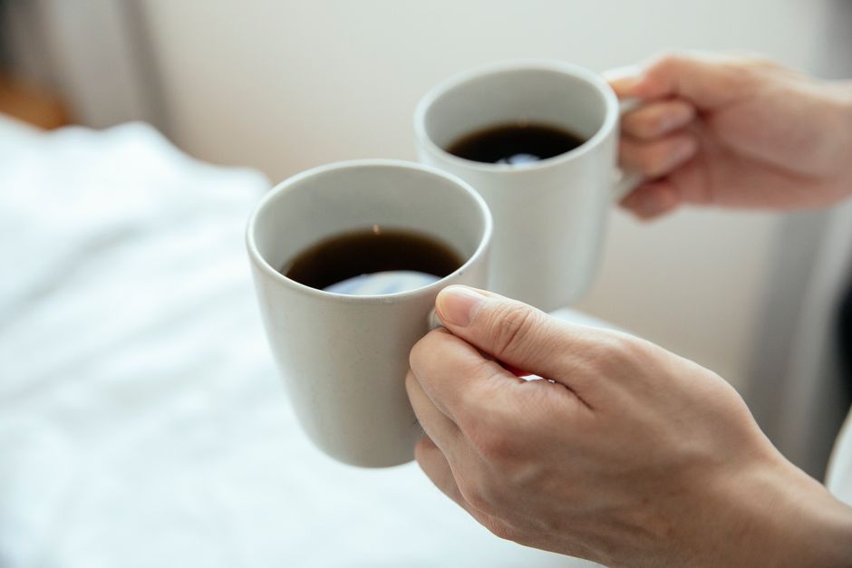 Close-up of hands holding two mugs filled with hot black coffee, perfect for a cozy morning.