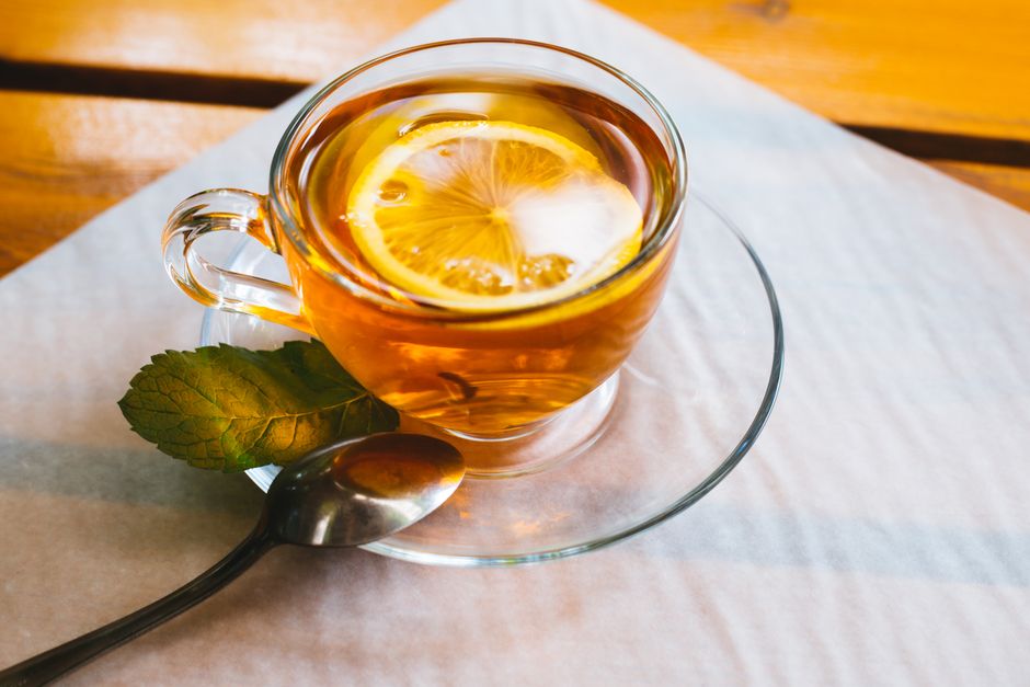 Close-up of lemon tea in a glass teacup with mint leaves and a spoon on a wooden table.
