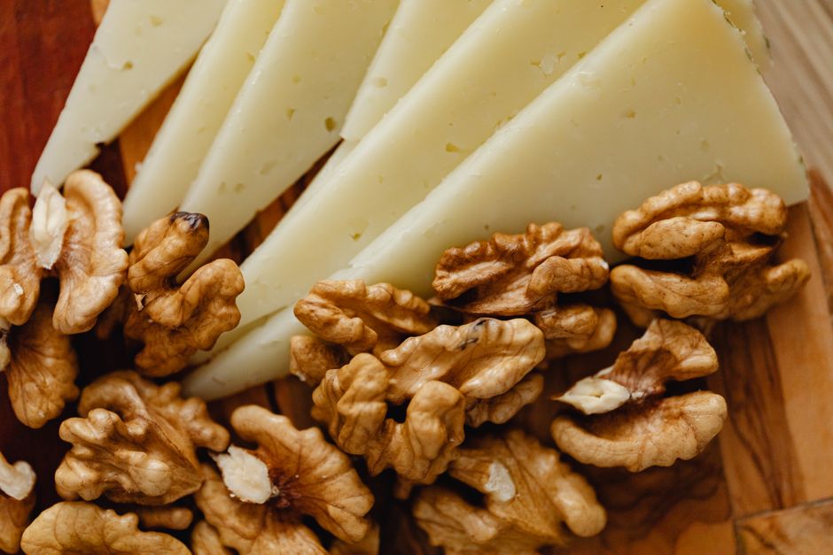 Close-up of sliced cheese with walnuts on a wooden board, ideal for appetizers.