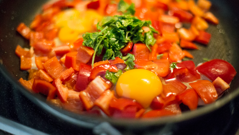 Close-up view of a colorful egg and bell pepper breakfast skillet with herbs.