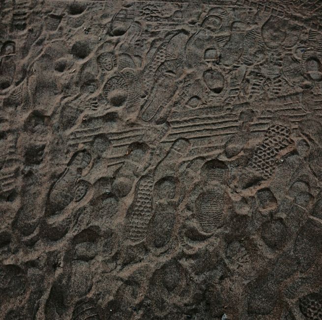 Close-up view of multiple footprints imprinted on sand at a beach, showing diverse textures.